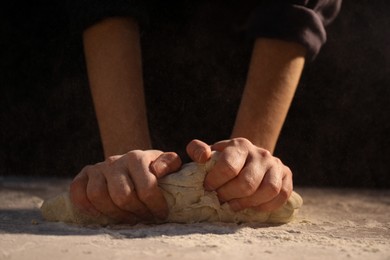 Photo of Making bread. Woman kneading dough at table on dark background, closeup