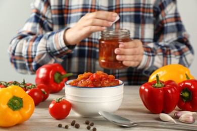 Photo of Tasty lecho, fresh ingredients and woman with jar at wooden table