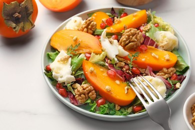 Photo of Delicious persimmon salad with cheese and pomegranate served on white table