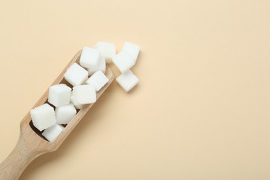 Photo of White sugar cubes and wooden scoop on beige background, top view. Space for text