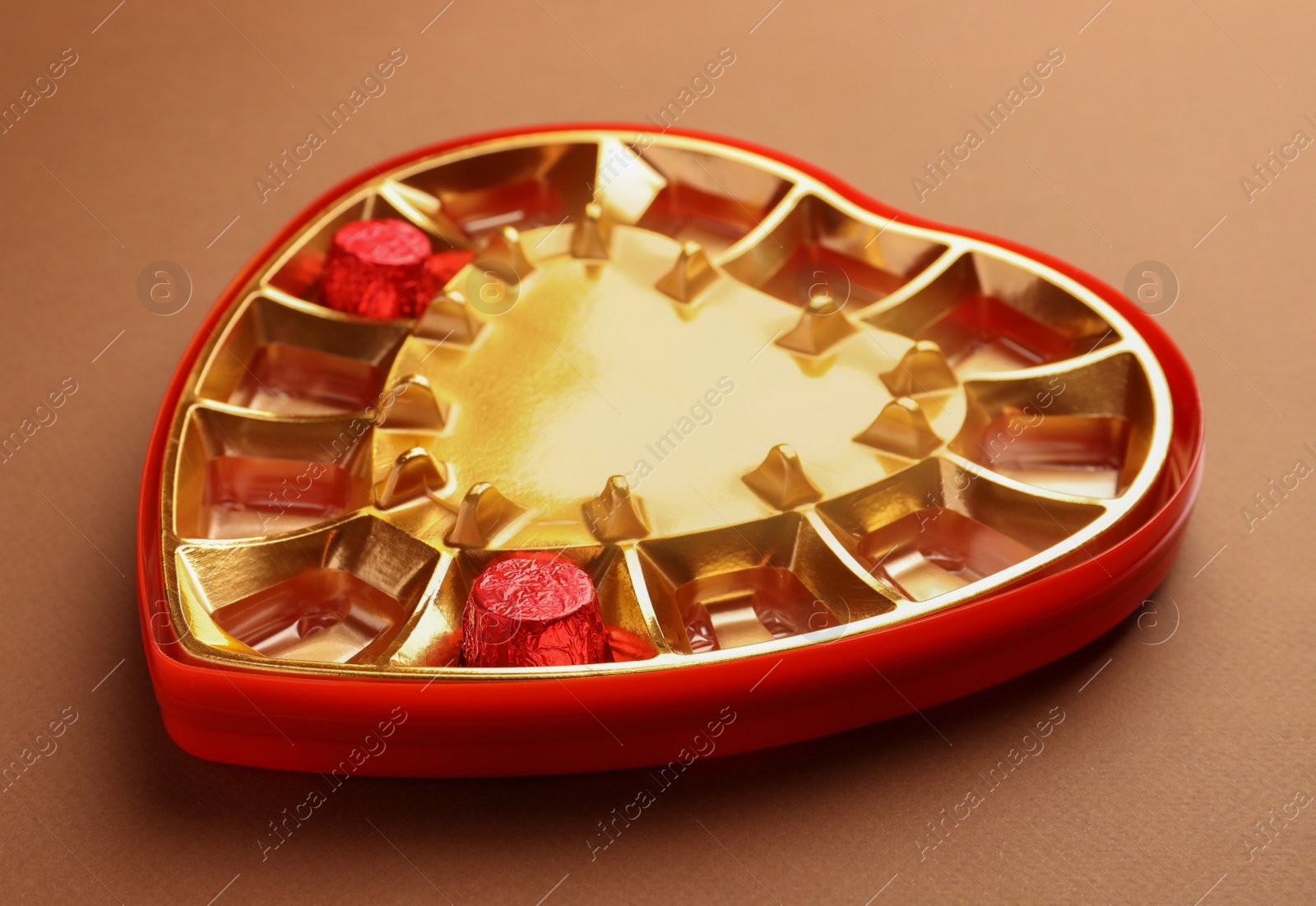 Photo of Partially empty heart shaped box of chocolate candies on brown background