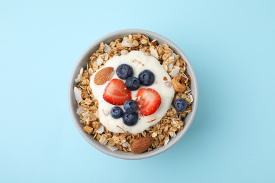 Photo of Tasty granola, yogurt and fresh berries in bowl on light blue background, top view. Healthy breakfast