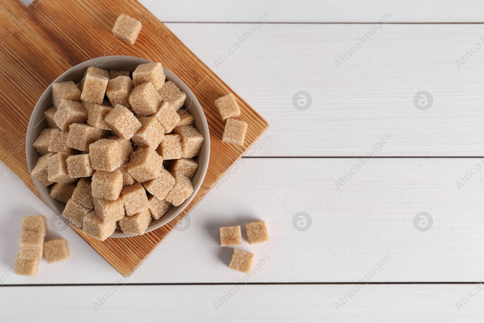 Photo of Brown sugar cubes on white wooden table, flat lay. Space for text