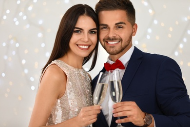 Photo of Lovely young couple with glasses of champagne against blurred festive lights. Christmas celebration