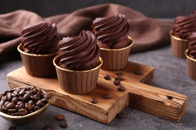 Photo of Delicious chocolate cupcakes and coffee beans on grey textured table, closeup