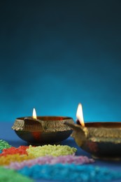 Photo of Diwali celebration. Diya lamps and colorful rangoli on blue background, closeup. Space for text