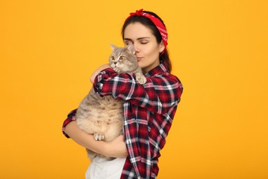 Photo of Young woman kissing her adorable cat on yellow background, space for text