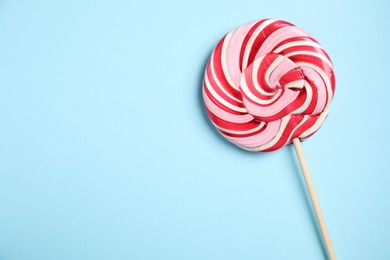 Photo of Stick with colorful lollipop swirl on light blue background, top view. Space for text