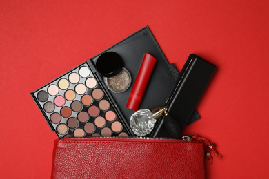 Photo of Cosmetic bag with makeup products and perfume on red background, flat lay