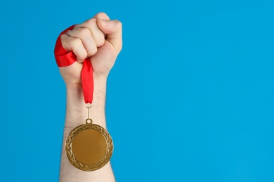 Photo of Man holding golden medal on blue background, closeup. Space for design