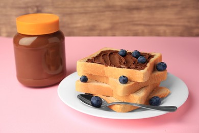 Photo of Tasty toast with chocolate paste and blueberries near jar on pink table