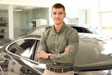 Photo of Young man near new car in modern auto dealership