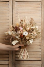 Photo of Woman holding beautiful dried flower bouquet on wooden background, closeup