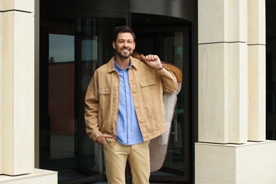 Photo of Attractive happy man holding garment cover with clothes outdoors. Dry cleaning service