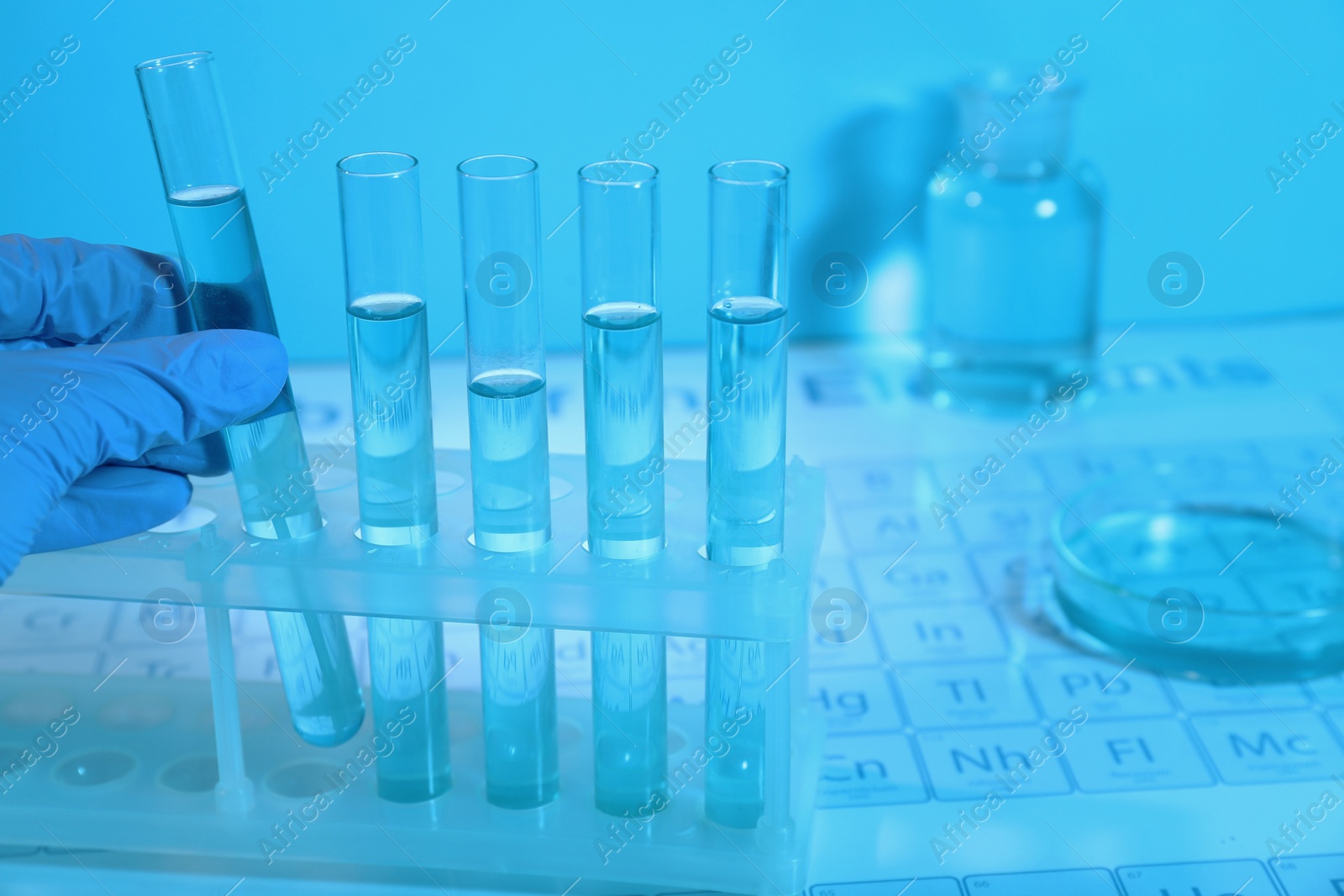 Photo of Scientist taking test tube with liquid from rack on periodic table of elements in laboratory, closeup. Color tone effect