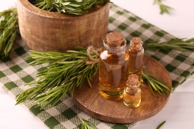 Photo of Essential oil in bottles and rosemary on white wooden table