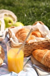 Photo of Blanket with juice and croissants for picnic on green grass, closeup