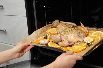 Photo of Woman putting chicken with orange slices into oven, closeup