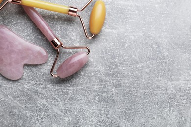 Photo of Quartz gua sha tool and face rollers on grey background, flat lay. Space for text