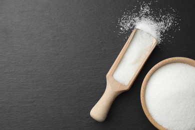 Photo of Granulated sugar in bowl and scoop on black table, flat lay. Space for text
