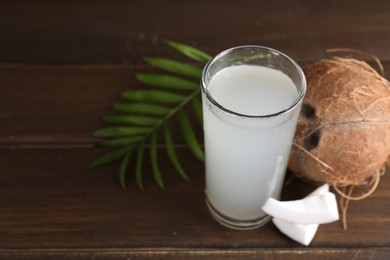 Photo of Glass of coconut water, leaf and nuts on wooden table, space for text