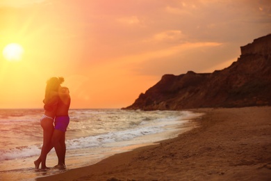 Photo of Young woman in bikini and her boyfriend on beach at sunset. Lovely couple
