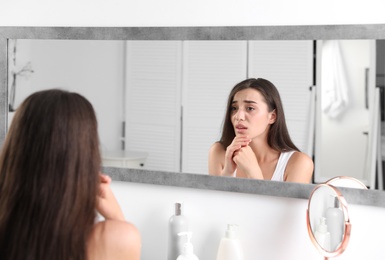 Photo of Young woman with eyelash loss problem looking in mirror indoors