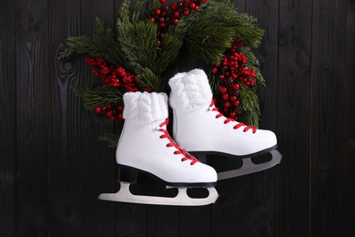 Photo of Pair of ice skates and beautiful Christmas wreath hanging on dark wooden wall