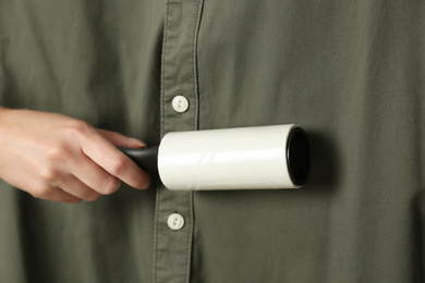 Photo of Woman cleaning khaki shirt with lint roller, closeup