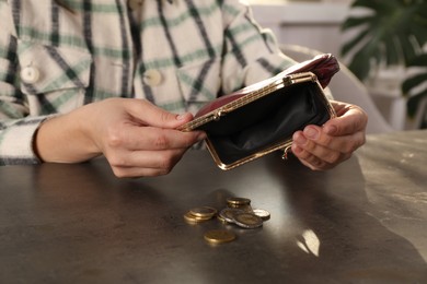 Photo of Poor woman pouring coins out of wallet at grey table indoors, closeup