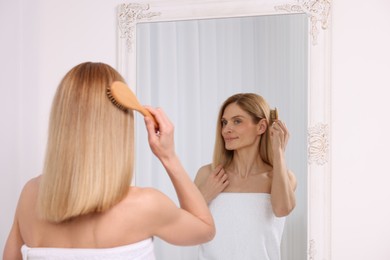 Photo of Beautiful woman brushing her hair near mirror in room