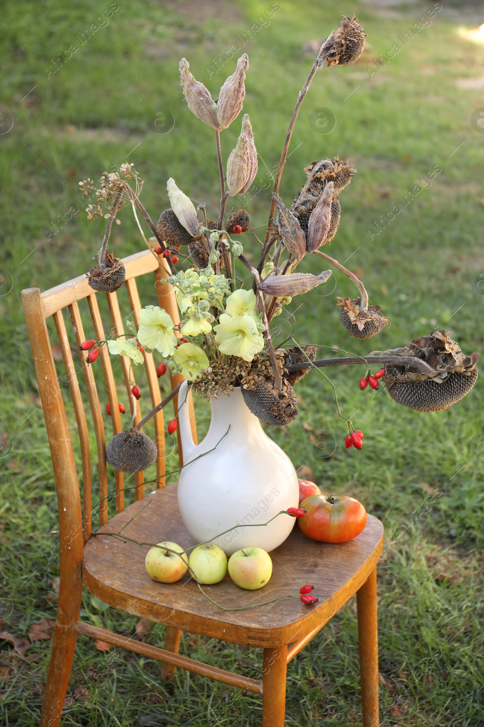 Photo of Composition with beautiful flowers, dry sunflowers and apples on wooden chair outdoors. Autumn atmosphere