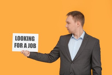 Photo of Unemployed man holding sign with phrase Looking For A Job on orange background