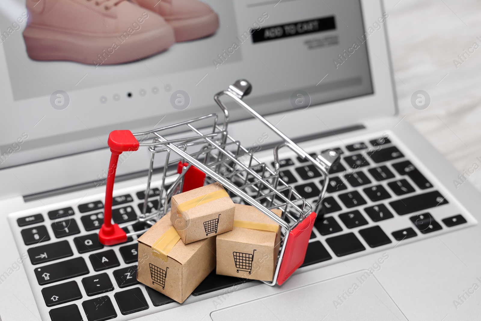 Image of Internet store. Small cardboard boxes, shopping cart and laptop on table