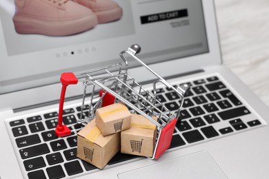 Image of Internet store. Small cardboard boxes, shopping cart and laptop on table