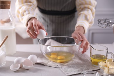 Making dough. Woman breaking egg at white table in kitchen, closeup