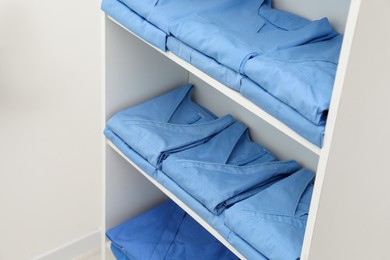 Light blue medical uniforms on white rack indoors