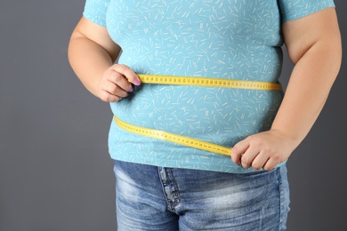 Photo of Overweight woman with measuring tape on gray background, closeup