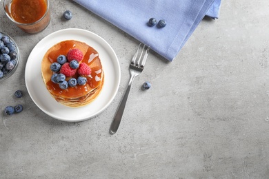 Tasty pancakes and berries served on grey table, flat lay. Space for text