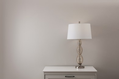 Photo of Wooden nightstand with lamp near white wall in room, space for text