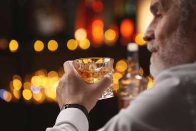 Photo of Senior man holding glass of whiskey with ice cubes in bar