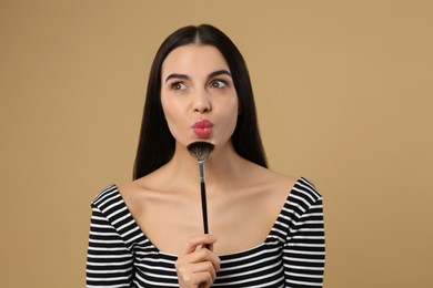 Woman with makeup brush on light brown background