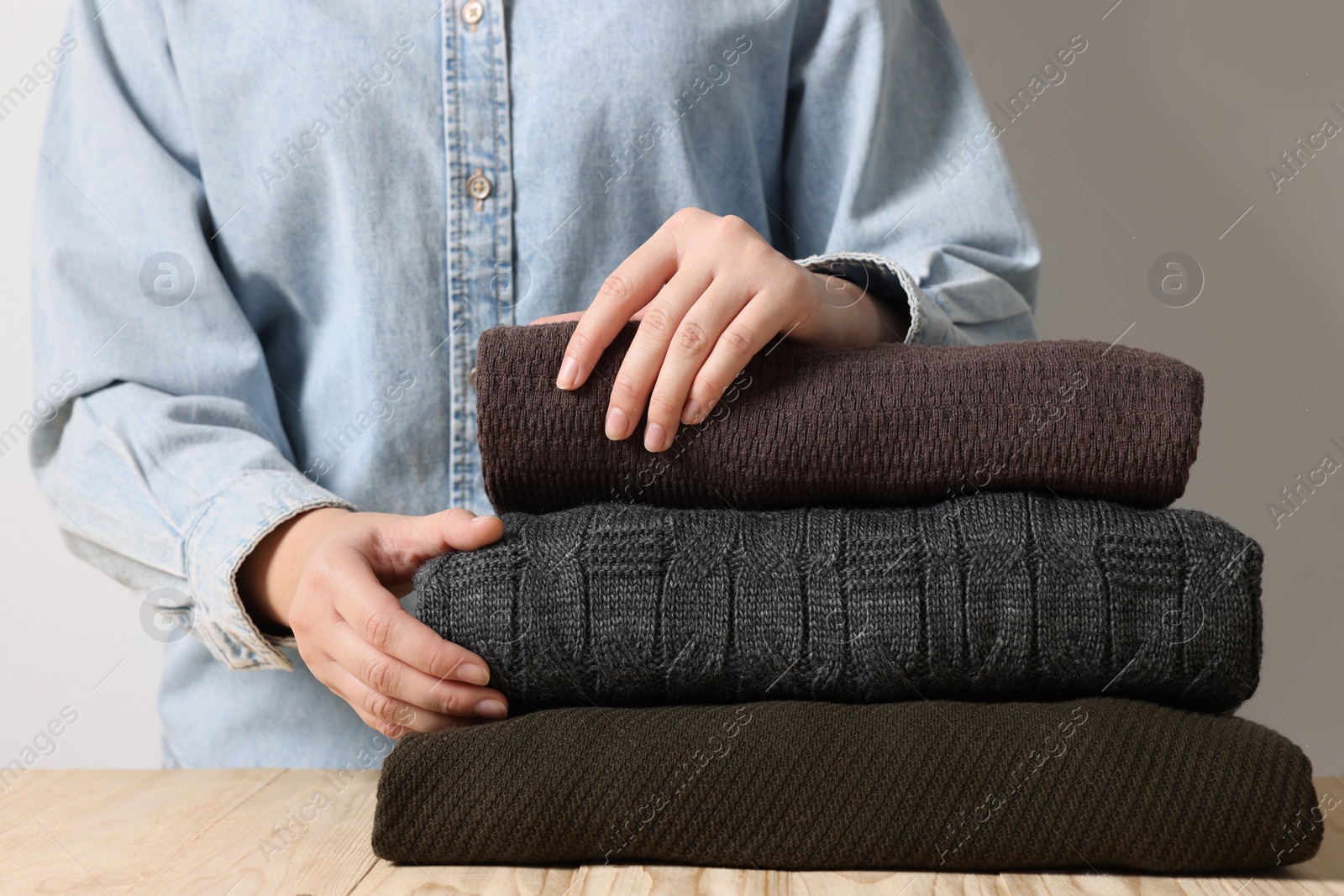 Photo of Woman with folded sweaters at wooden table on light background, closeup