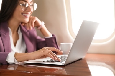 Photo of Young woman working with laptop on plane, closeup