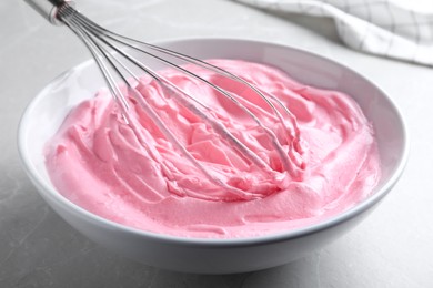 Photo of Whipping pink cream with balloon whisk on light grey table, closeup