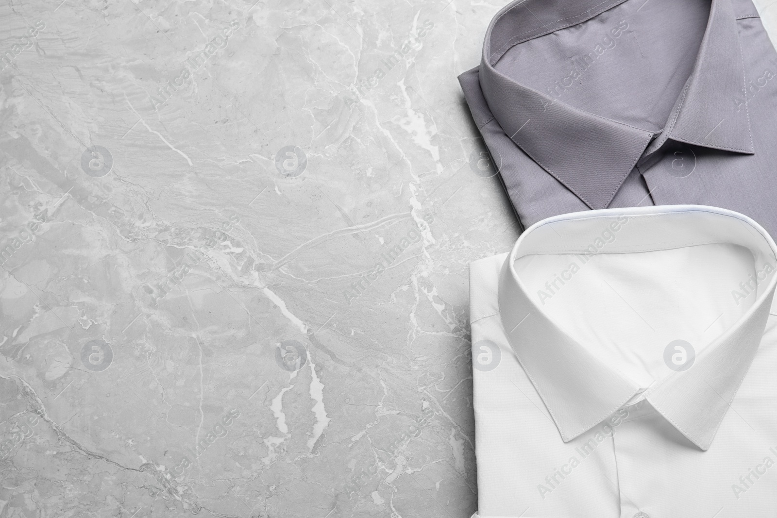 Photo of Stylish shirts on grey marble table, flat lay with space for text. Dry-cleaning service