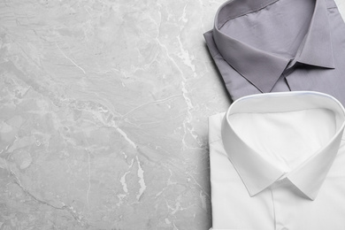 Stylish shirts on grey marble table, flat lay with space for text. Dry-cleaning service