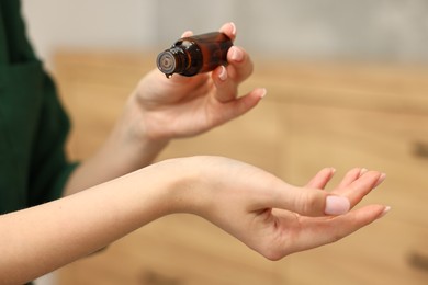 Aromatherapy. Woman with bottle of essential oil against blurred background, closeup