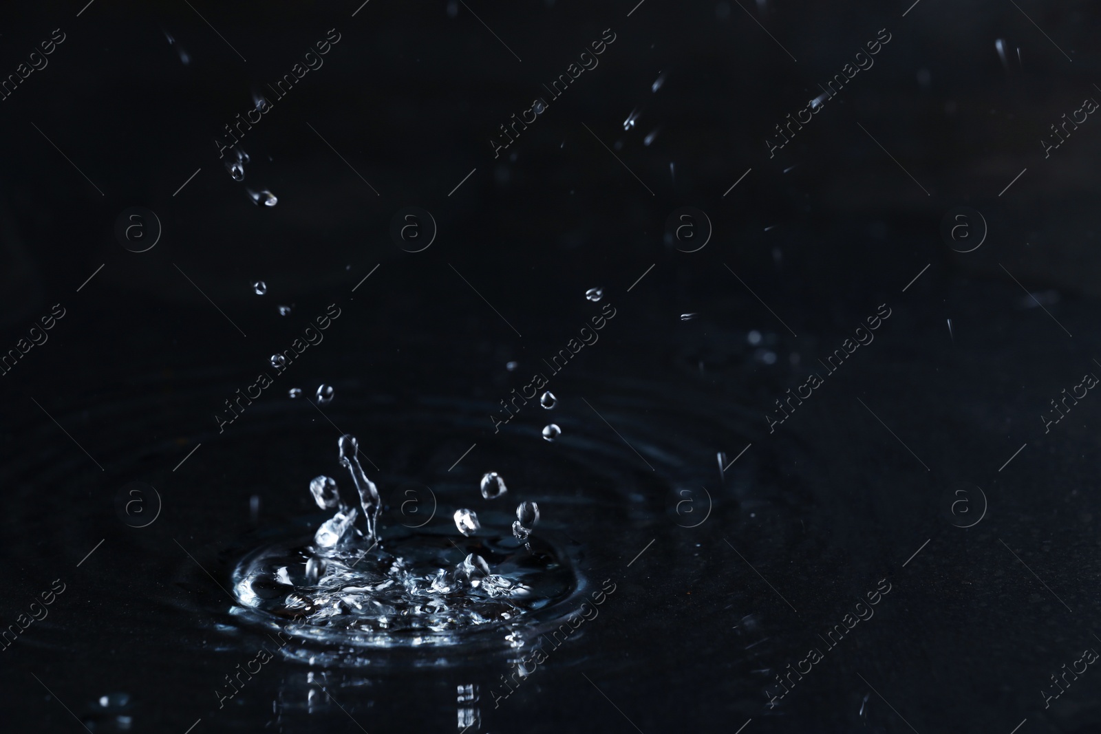 Photo of Rain drop falling down into puddle on dark background