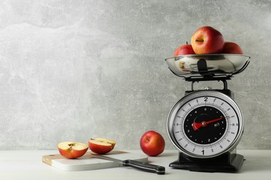 Photo of Kitchen scale with ripe apples on white wooden table. Space for text
